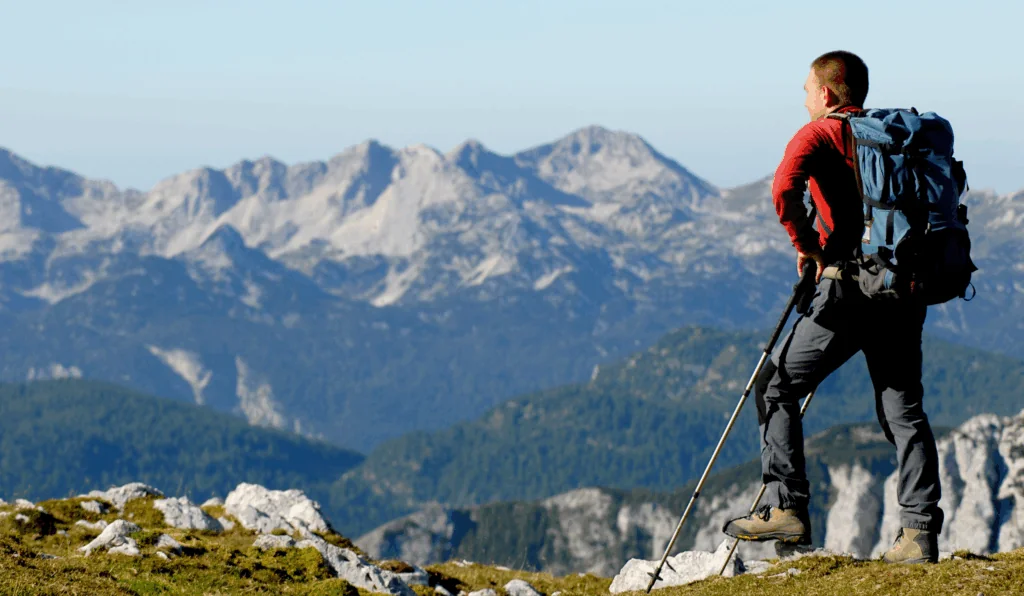 a hiker in full gear admiring the view at the top of a mountain trail