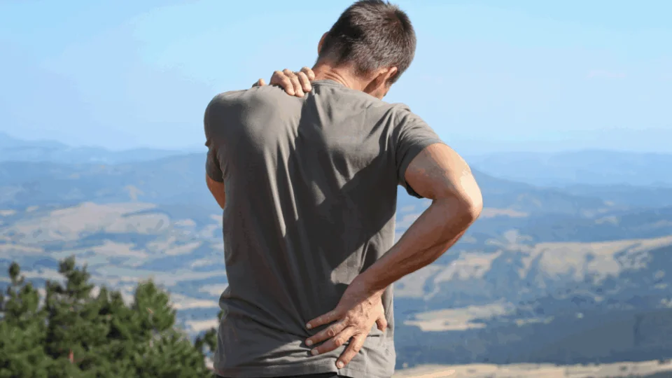 a hiker holding his back and neck on the hiking trail